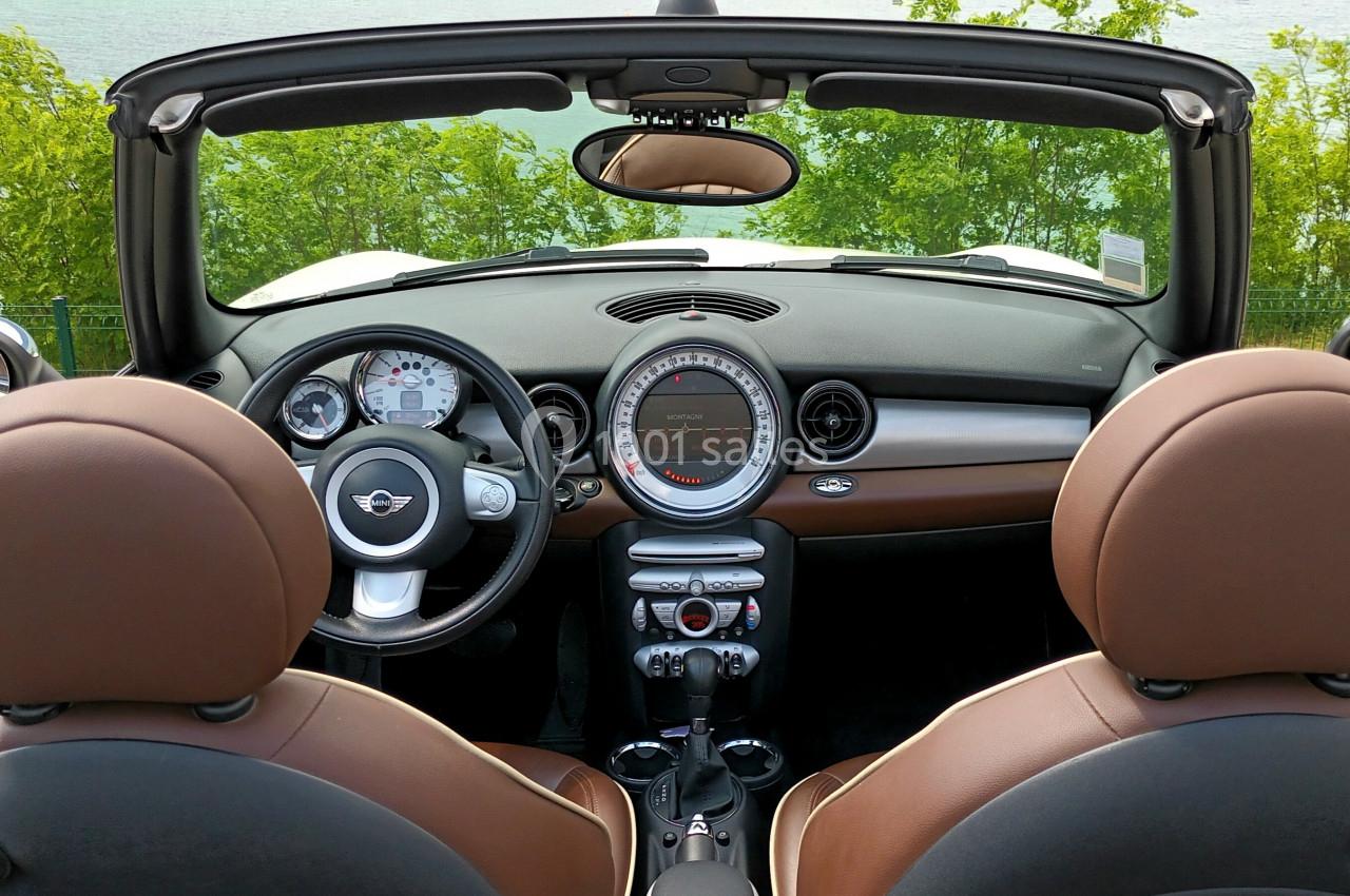 Vue intérieure d'une voiture décapotable avec sièges en cuir marron, tableau de bord moderne et paysage verdoyant en arrière…