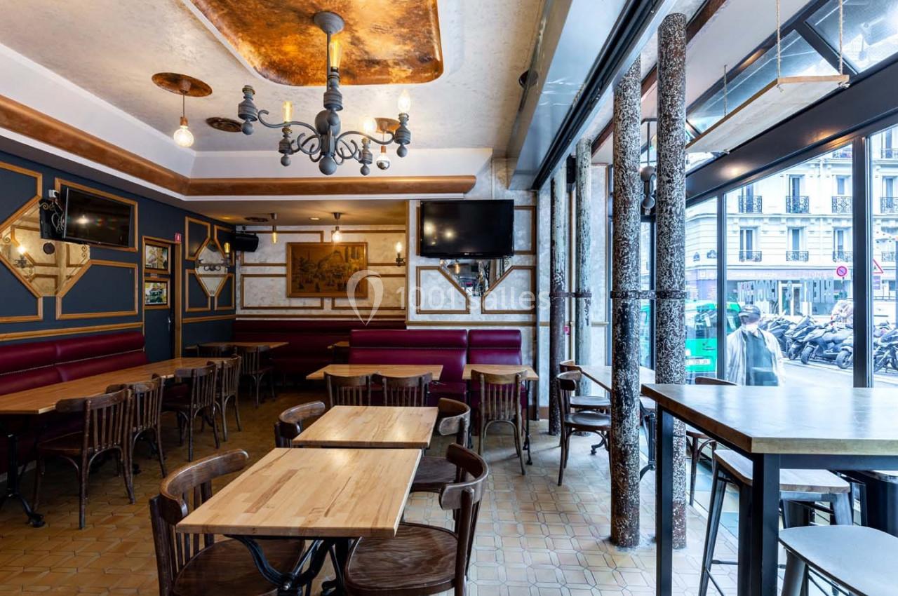Salle de restaurant lumineuse avec tables en bois, chaises assorties, décorations murales et grandes fenêtres donnant sur la…