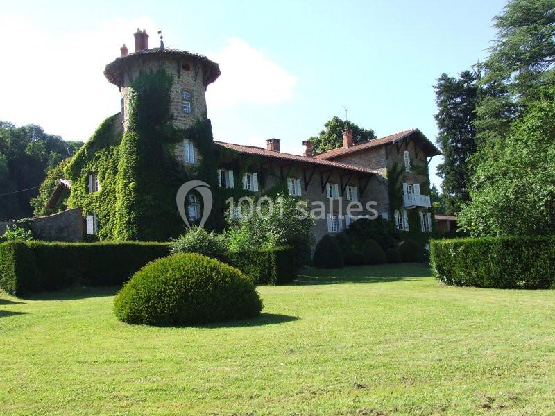 Manoir en pierre recouvert de lierre, entouré d'un jardin bien entretenu avec pelouse et arbustes taillés.