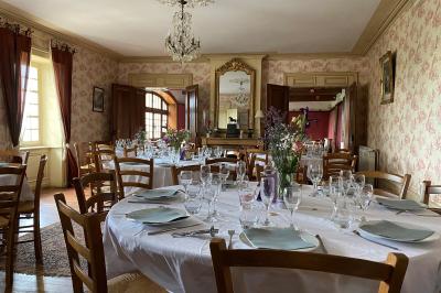 Salle de restaurant avec tables rondes dressées, nappes blanches, chaises en bois et éclairage tamisé.