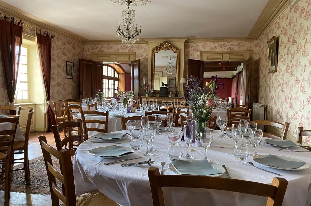 Salle à manger élégante avec tables rondes dressées, nappes blanches, vaisselle raffinée et décoration florale.