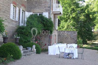 Salle de restaurant avec tables rondes dressées, nappes blanches, chaises en bois et éclairage tamisé.