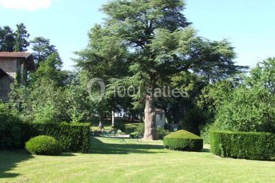 Salle de restaurant avec tables rondes dressées, nappes blanches, chaises en bois et éclairage tamisé.