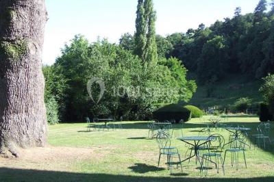 Salle de restaurant avec tables rondes dressées, nappes blanches, chaises en bois et éclairage tamisé.
