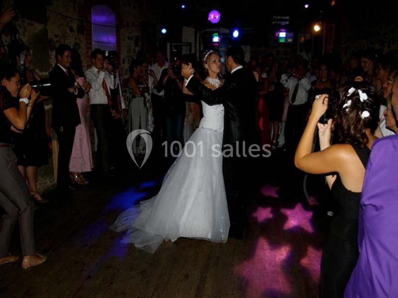 Un couple de mariés danse au centre d'une salle sombre entourée d'invités debout.