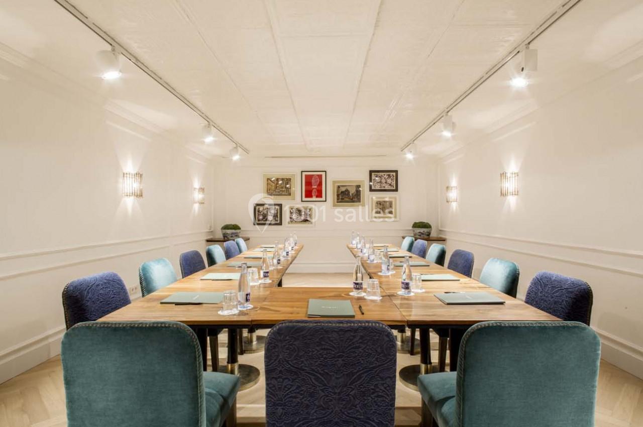 Salle de réunion lumineuse avec une grande table en bois, chaises bleues et décorations murales encadrées.