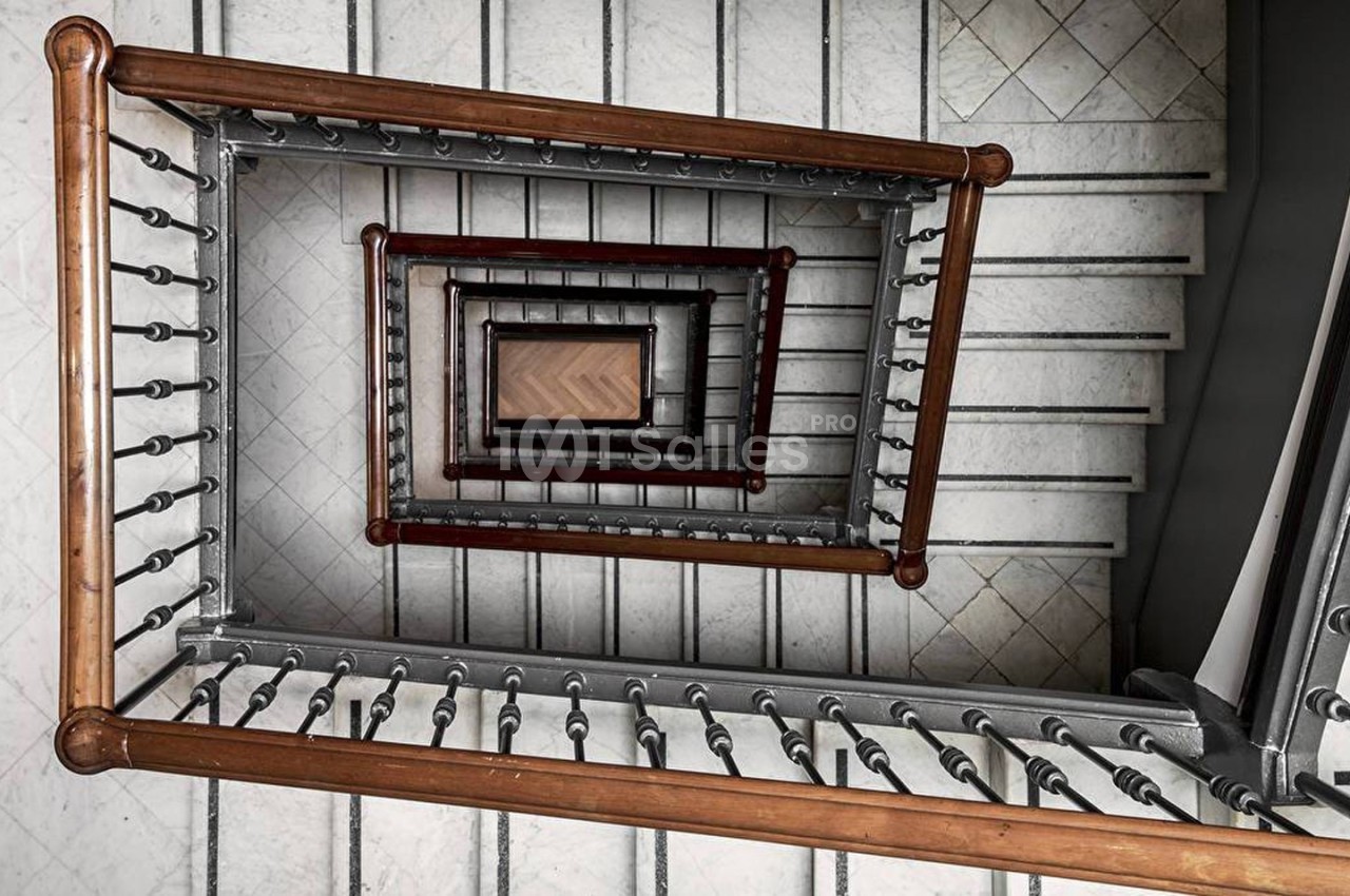 Vue plongeante d'une cage d'escalier en colimaçon avec rambardes en métal et marches en bois.