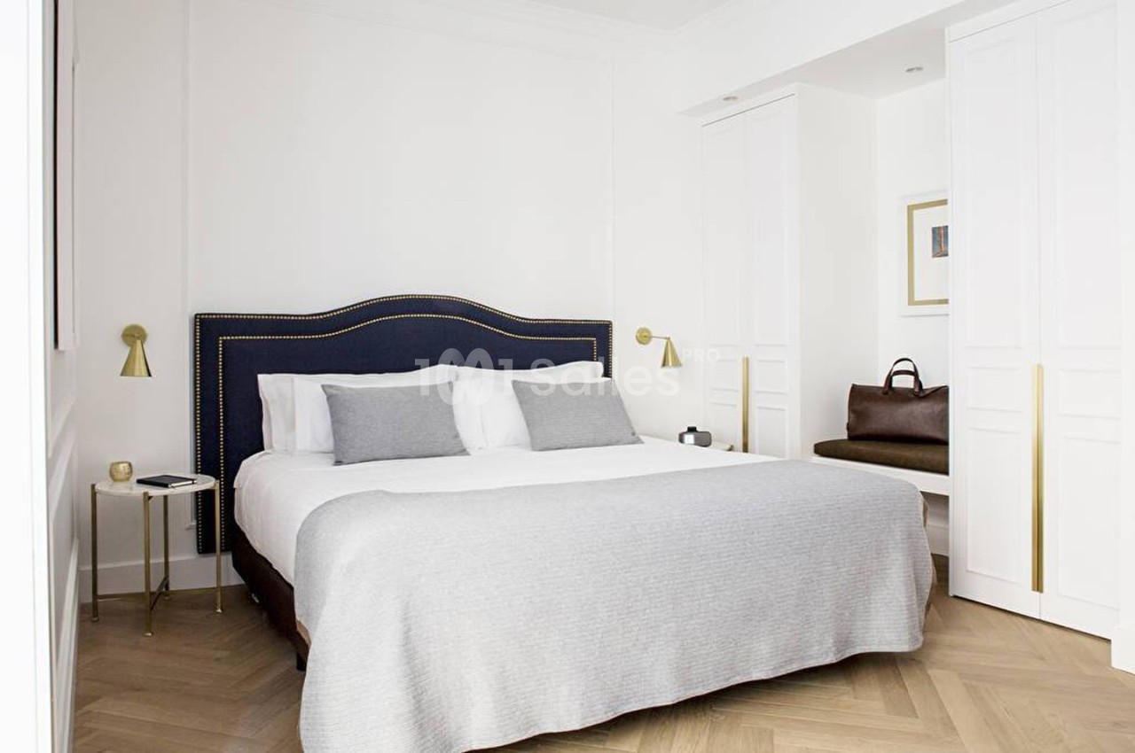 Chambre lumineuse avec lit double, tête de lit bleue, coussins gris, parquet en bois clair et placards blancs.