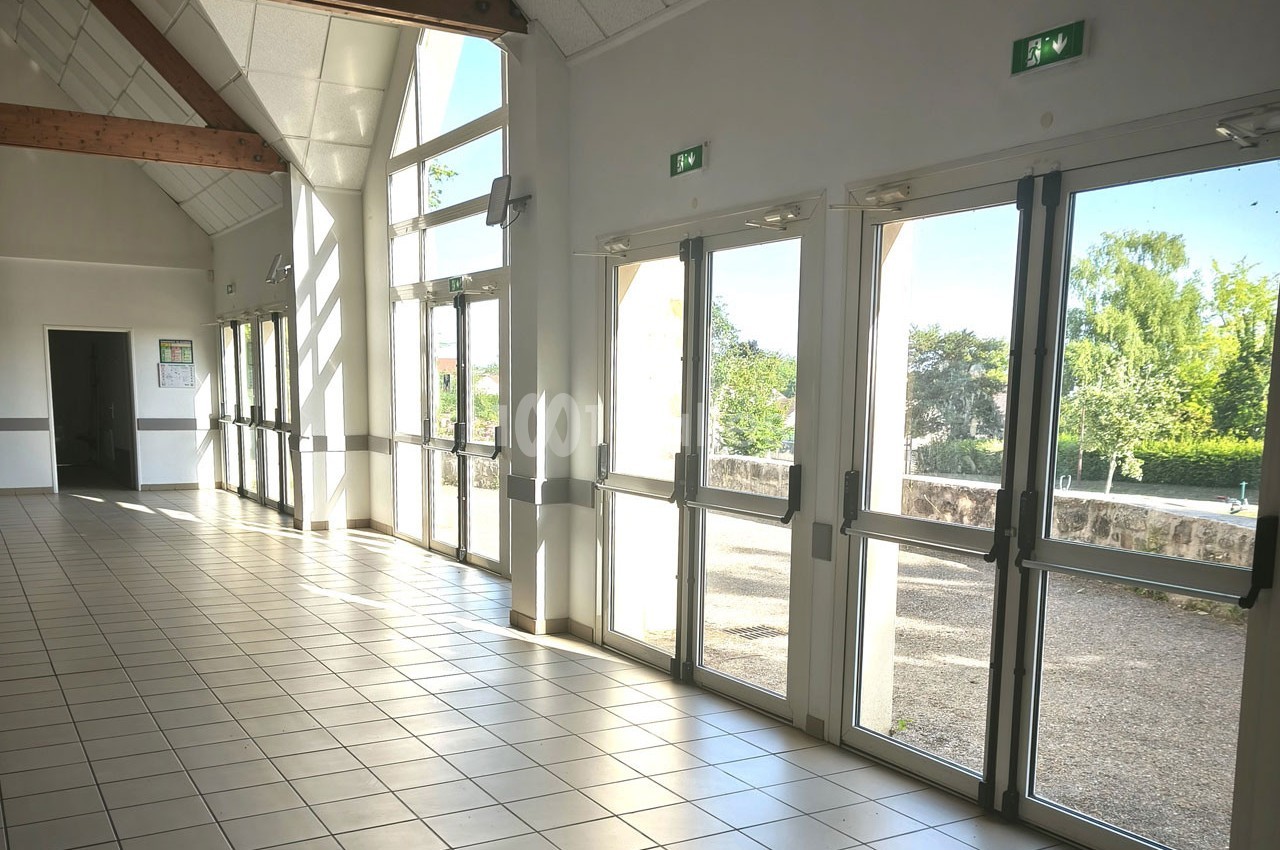 Vue intérieure d'une salle lumineuse avec de grandes baies vitrées donnant sur un espace extérieur arboré.