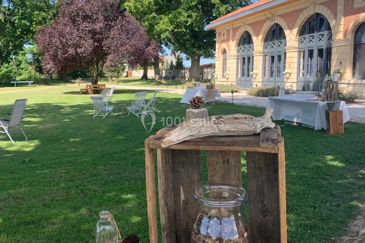 Location salle Cleppé (Loire) - L'Orangerie de Châtel #3 Table décorative en bois avec des éléments naturels, dans un jardin verdoyant près d'un bâtiment en briques.