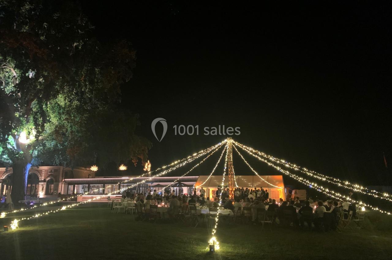 Location salle Cleppé (Loire) - L'Orangerie de Châtel #20 Tente éclairée par des guirlandes lumineuses dans un jardin, entourée de convives en soirée.