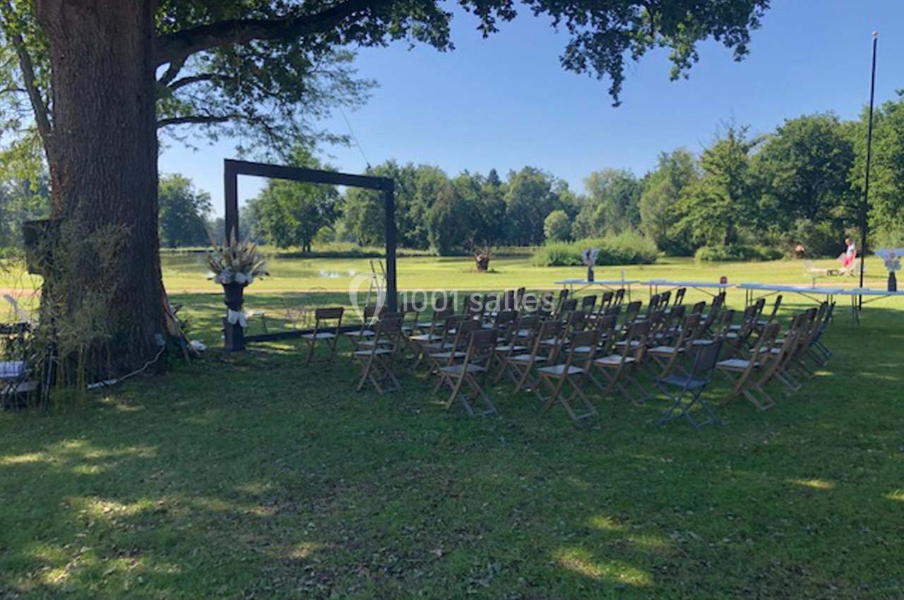 Location salle Cleppé (Loire) - L'Orangerie de Châtel #11 Chaises en bois disposées en rangées sous un grand arbre, formant un espace extérieur pour une cérémonie.