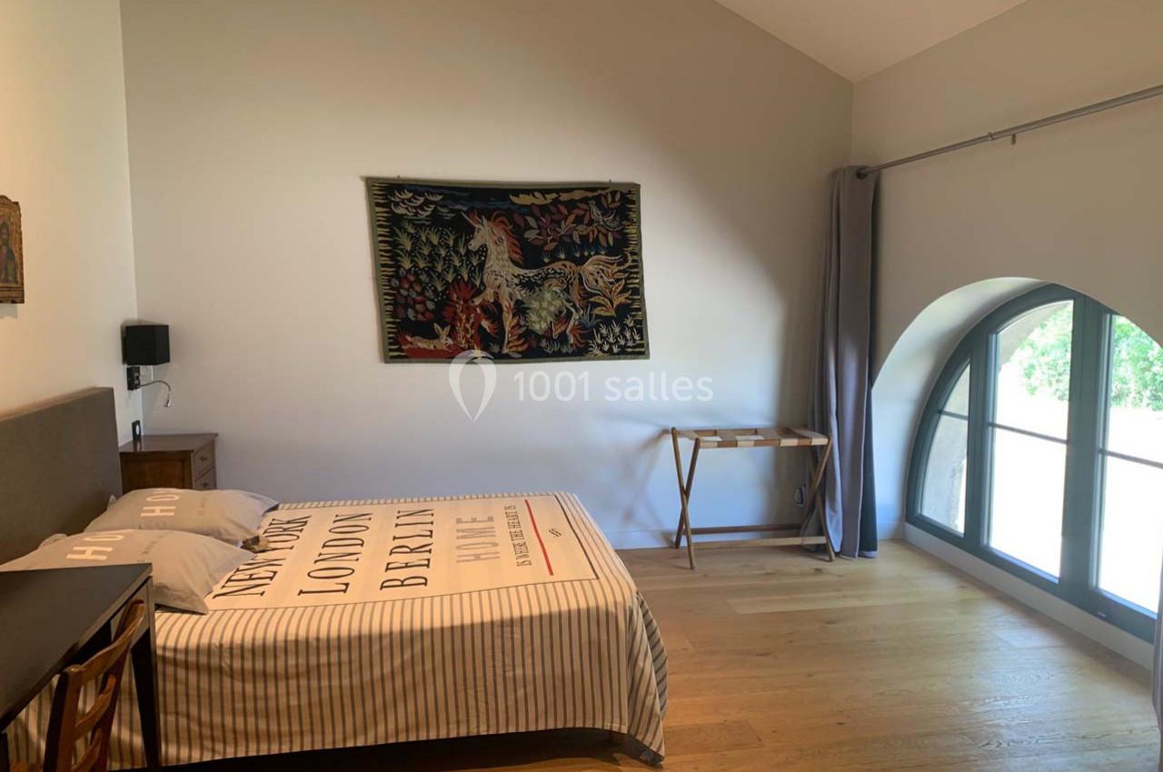 Location salle Cleppé (Loire) - L'Orangerie de Châtel #29 Chambre lumineuse avec un lit double, une tapisserie murale, un bureau en bois et une grande fenêtre cintrée.
