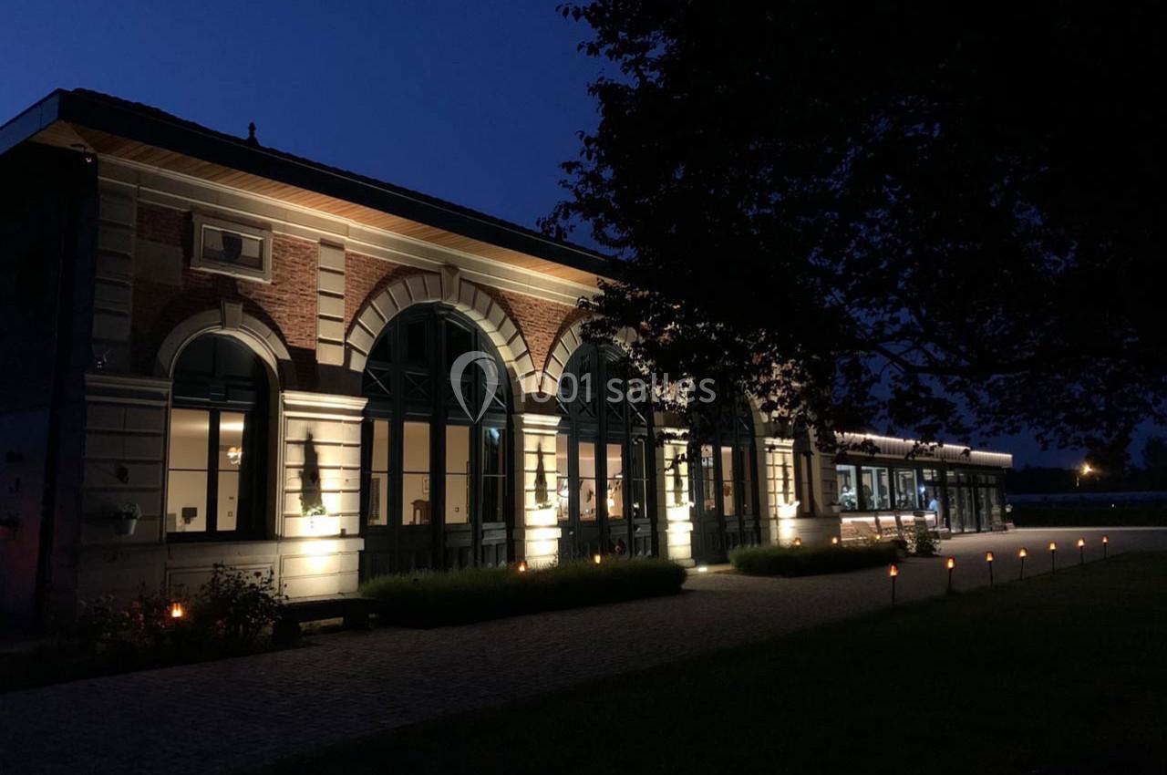 Location salle Cleppé (Loire) - L'Orangerie de Châtel #21 Bâtiment en briques et pierres éclairé la nuit, avec de grandes fenêtres et un arbre au premier plan.