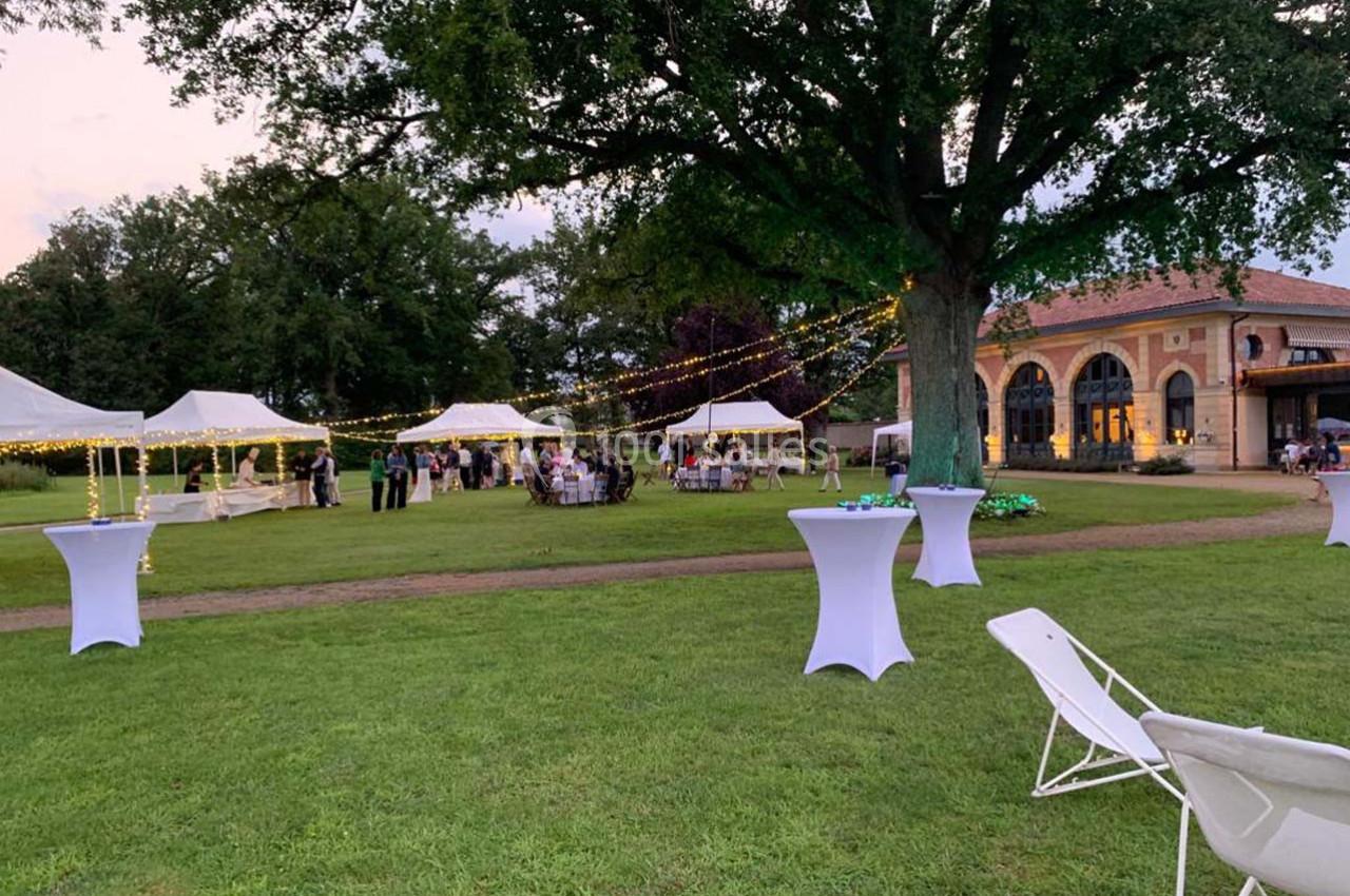 Location salle Cleppé (Loire) - L'Orangerie de Châtel #4 Jardin avec tentes blanches, guirlandes lumineuses et tables hautes lors d'un événement en plein air au crépuscule.
