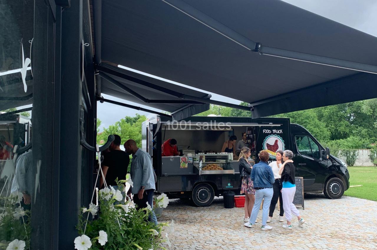 Location salle Cleppé (Loire) - L'Orangerie de Châtel #23 Un food truck noir stationné sur une allée pavée, des personnes commandent et discutent à proximité.