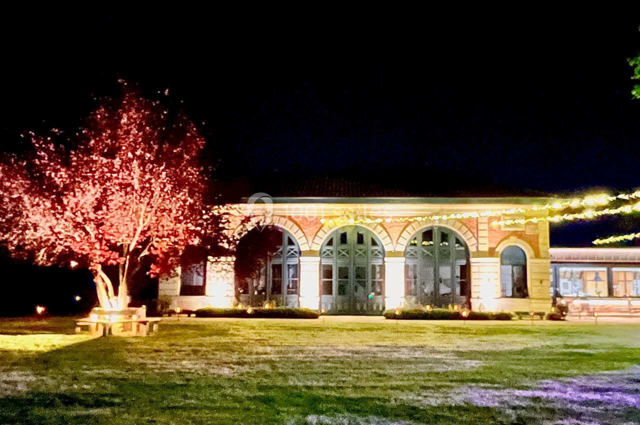Location salle Cleppé (Loire) - L'Orangerie de Châtel #33 Bâtiment en briques éclairé la nuit, entouré d'arbres illuminés et d'une pelouse.