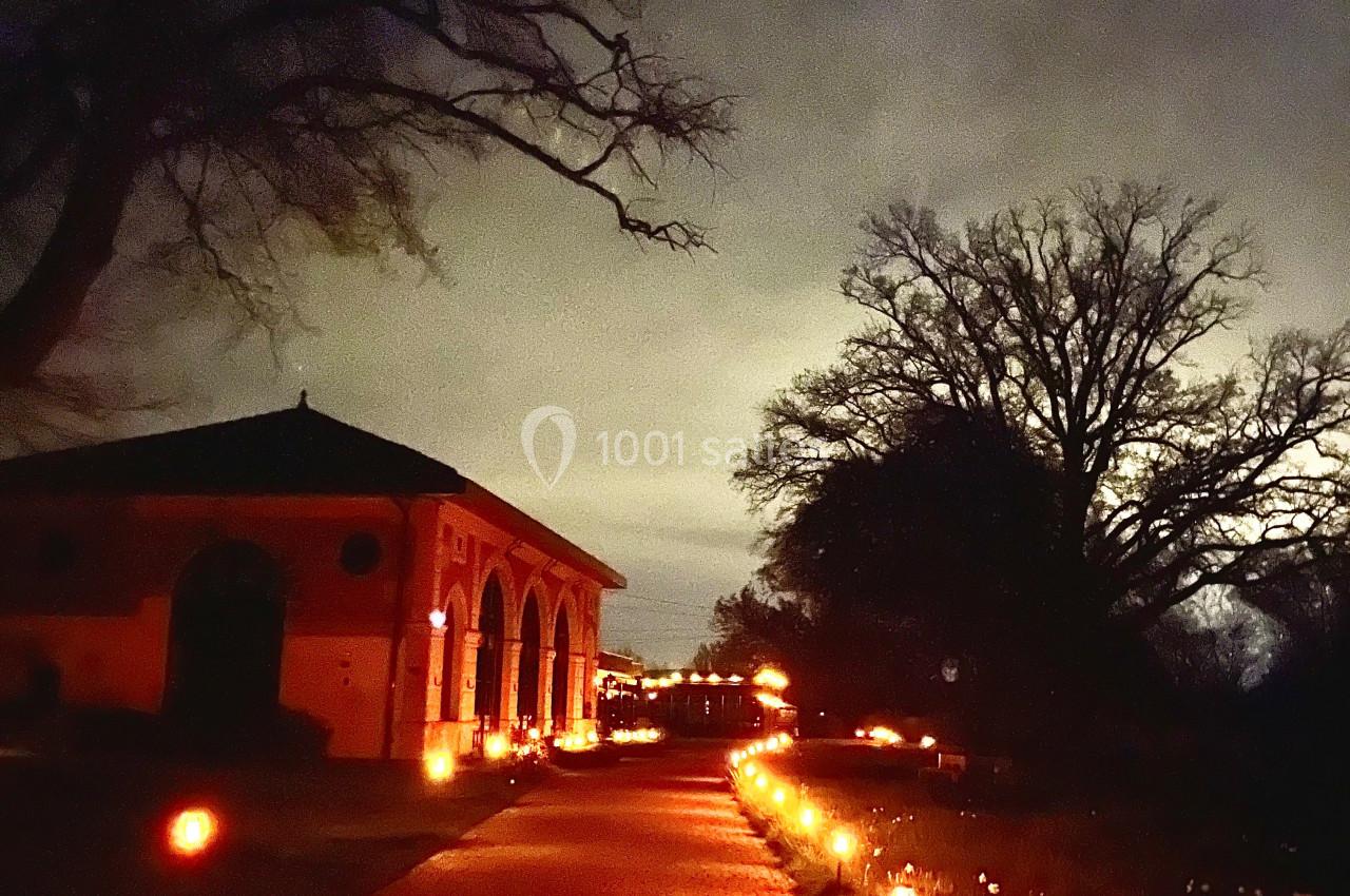 Location salle Cleppé (Loire) - L'Orangerie de Châtel #35 Allée pavée éclairée par des lanternes, bordée d'un bâtiment en briques et d'arbres sous un ciel nocturne.
