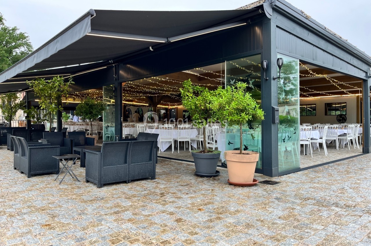 Location salle Cleppé (Loire) - L'Orangerie de Châtel #15 Terrasse couverte avec mobilier de jardin, entourée de plantes en pot, donnant sur une salle aménagée pour un événement.