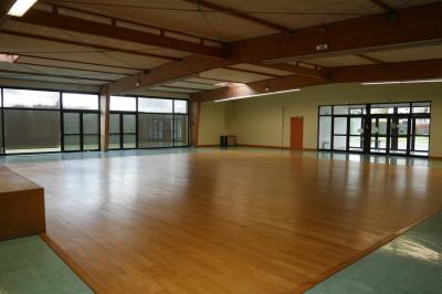 Salle de conférence vide avec des rangées de chaises noires, un écran de projection et des tables à l'avant.