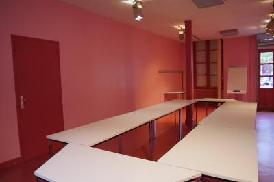 Salle de conférence vide avec des rangées de chaises noires, un écran de projection et des tables à l'avant.