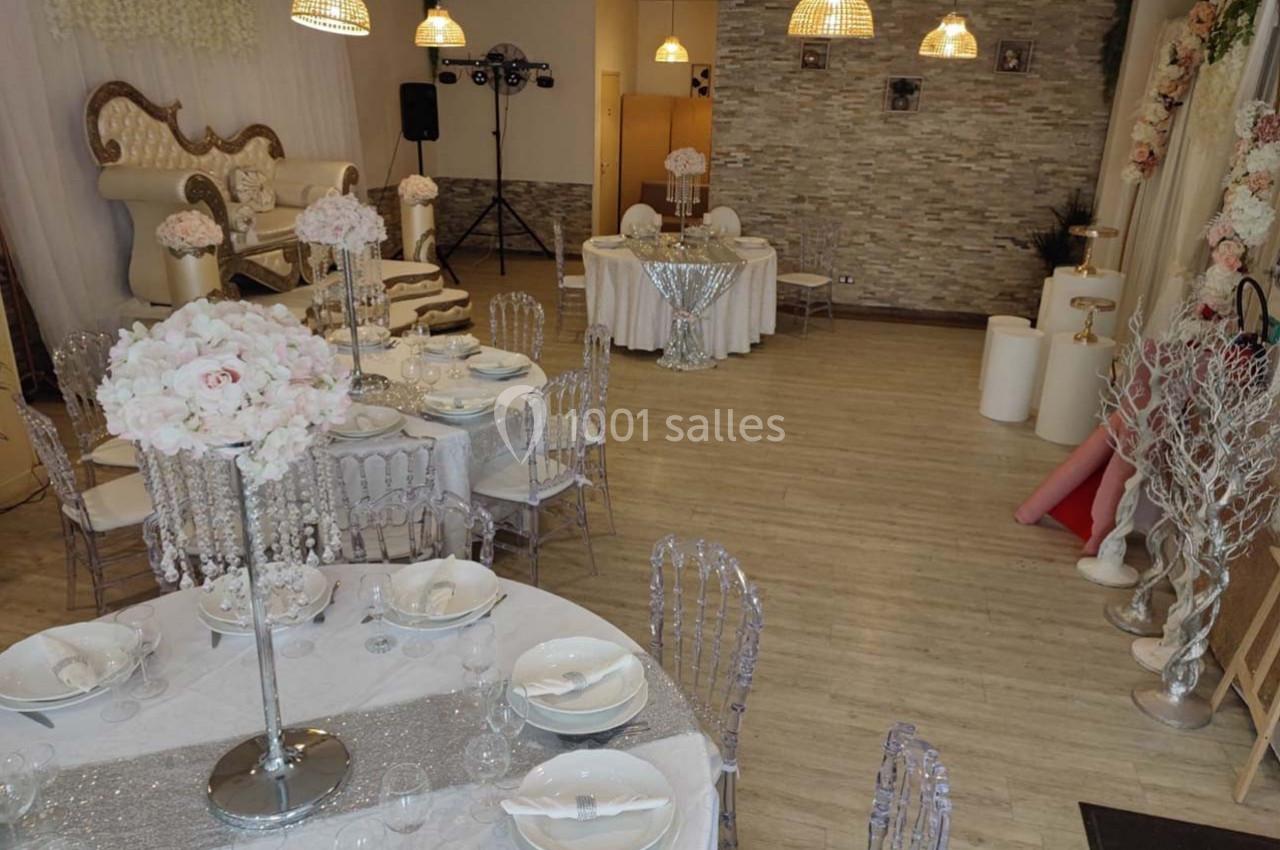 Salle de réception décorée avec des tables dressées, des chaises transparentes et des arrangements floraux élégants.