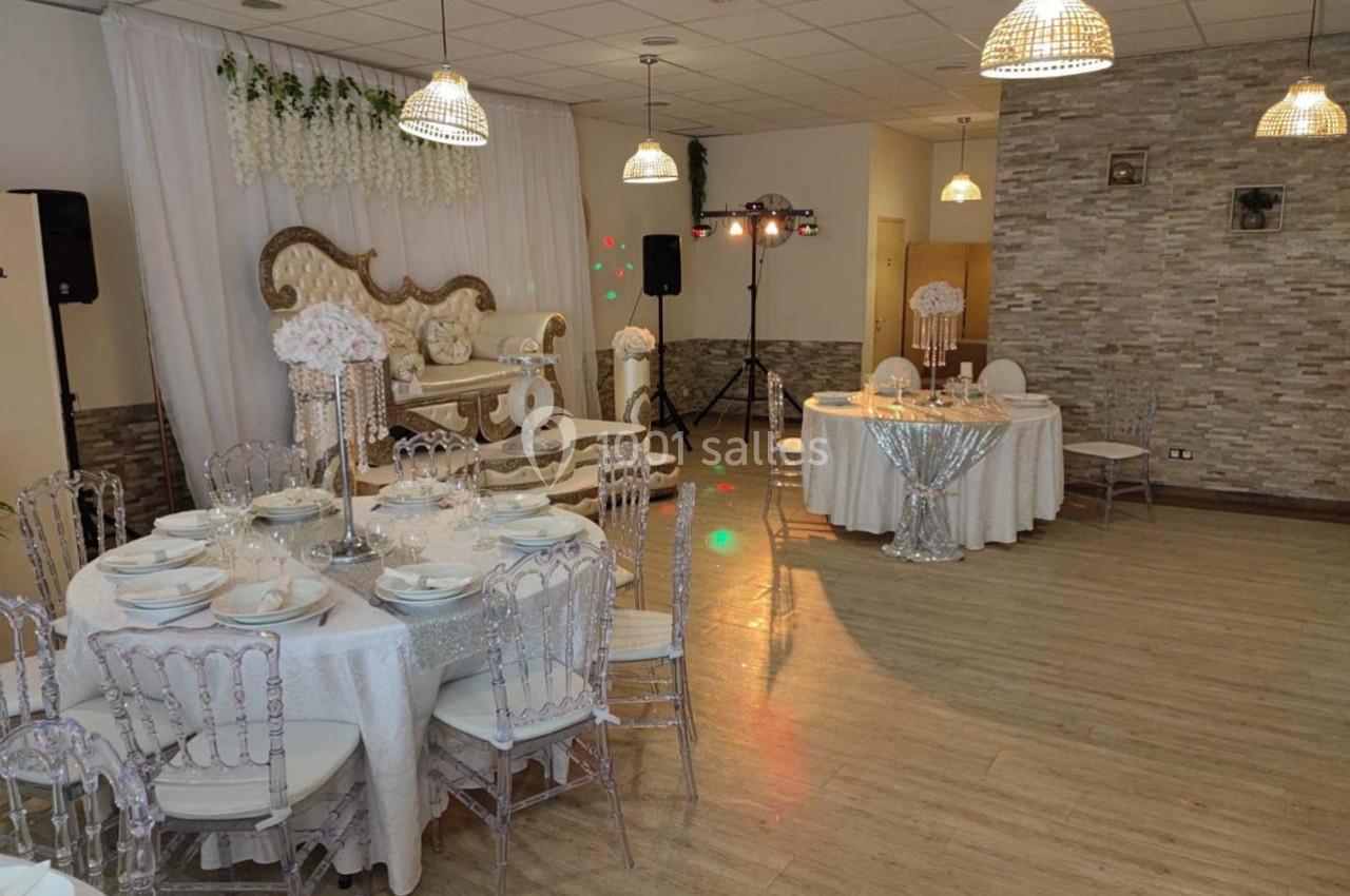 Salle de réception décorée avec des tables dressées, des chaises transparentes et un canapé orné sous un rideau blanc.
