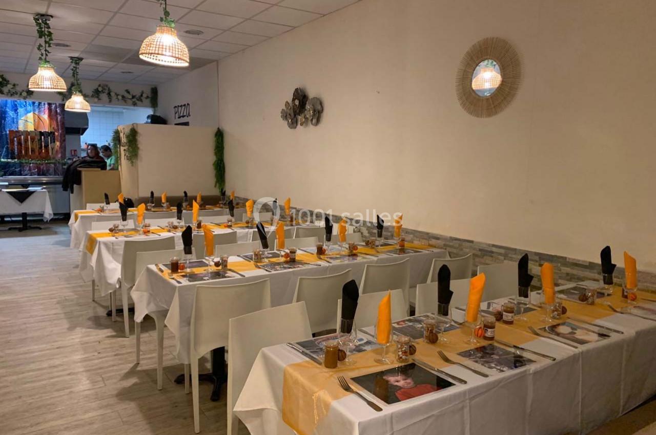 Salle de restaurant avec tables dressées, nappes blanches, serviettes orange et noires, éclairage chaleureux.