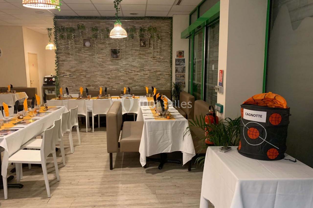 Salle de restaurant décorée avec des tables dressées et une urne marquée ’cagnotte’ posée sur une table.