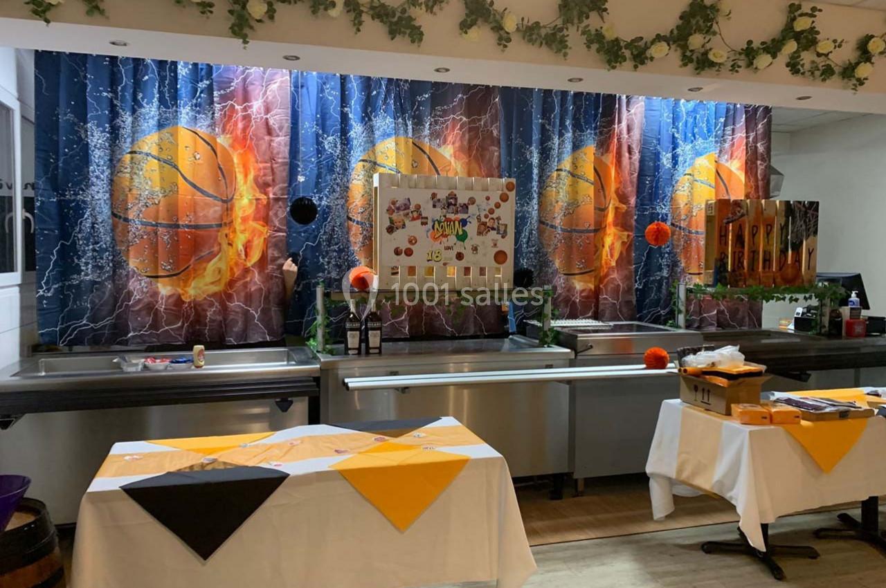 Décoration de salle avec thème basketball, rideaux illustrés de ballons enflammés, tables dressées avec nappes colorées.