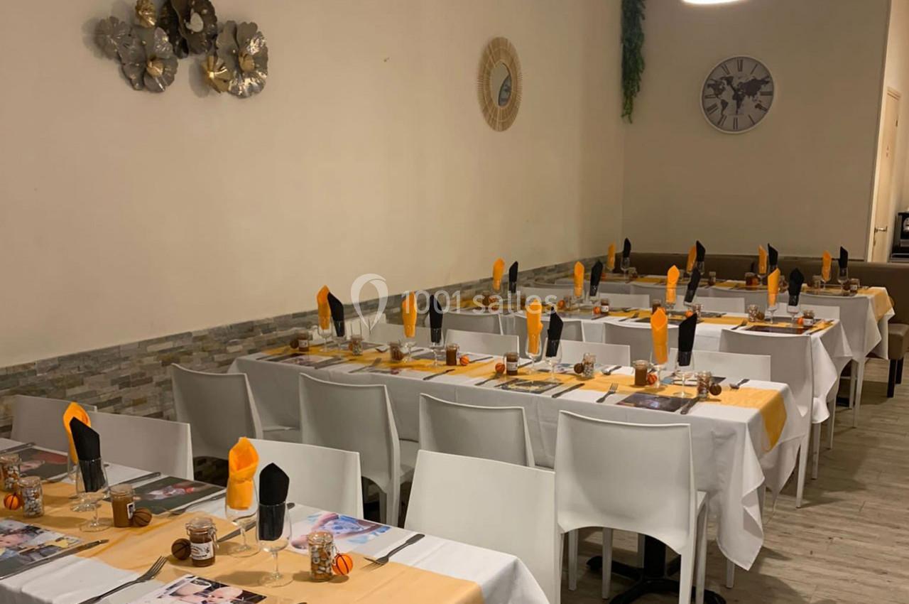 Salle de restaurant avec tables dressées, nappes blanches et jaunes, serviettes orange et noires, décor sobre.
