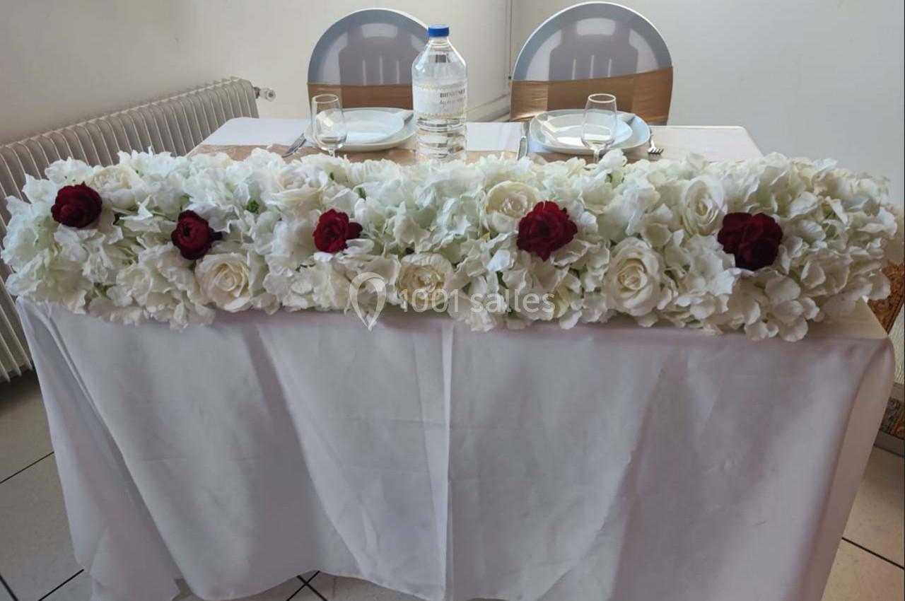 Décoration florale blanche et rouge ornant une table dressée avec deux chaises en arrière-plan.