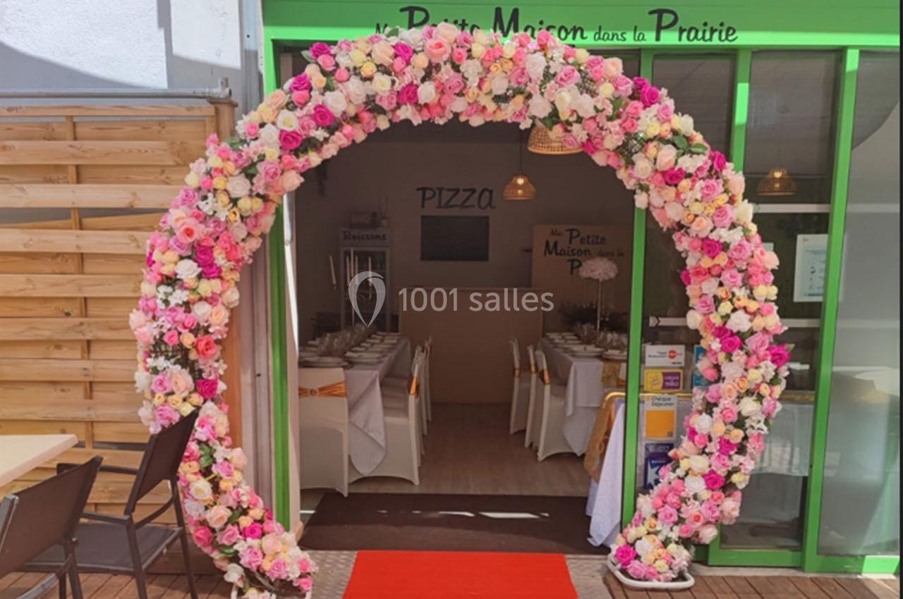 Arc floral coloré encadrant l'entrée d'un restaurant avec une table dressée visible à l'intérieur.