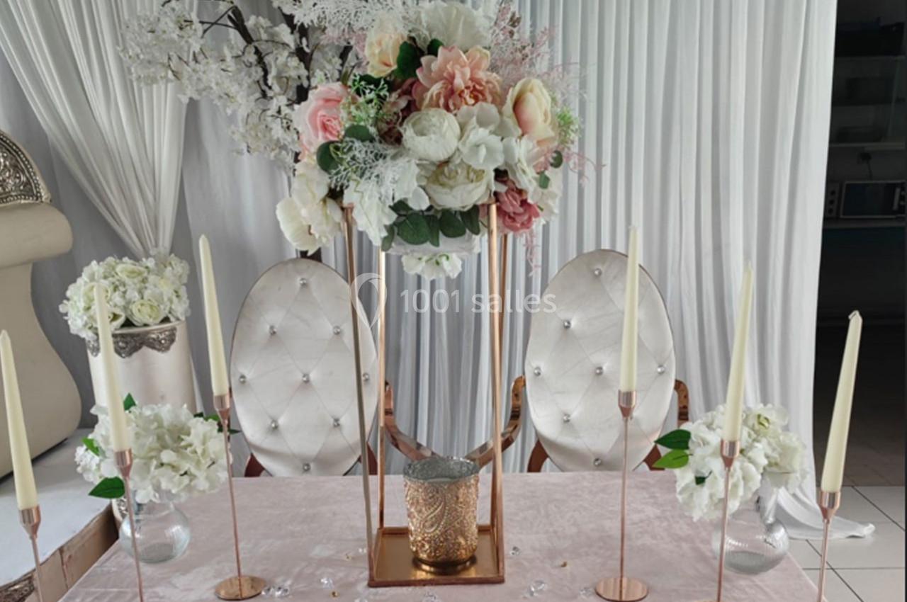 Décoration de table élégante avec fleurs blanches et roses, chandeliers dorés et chaises capitonnées blanches.