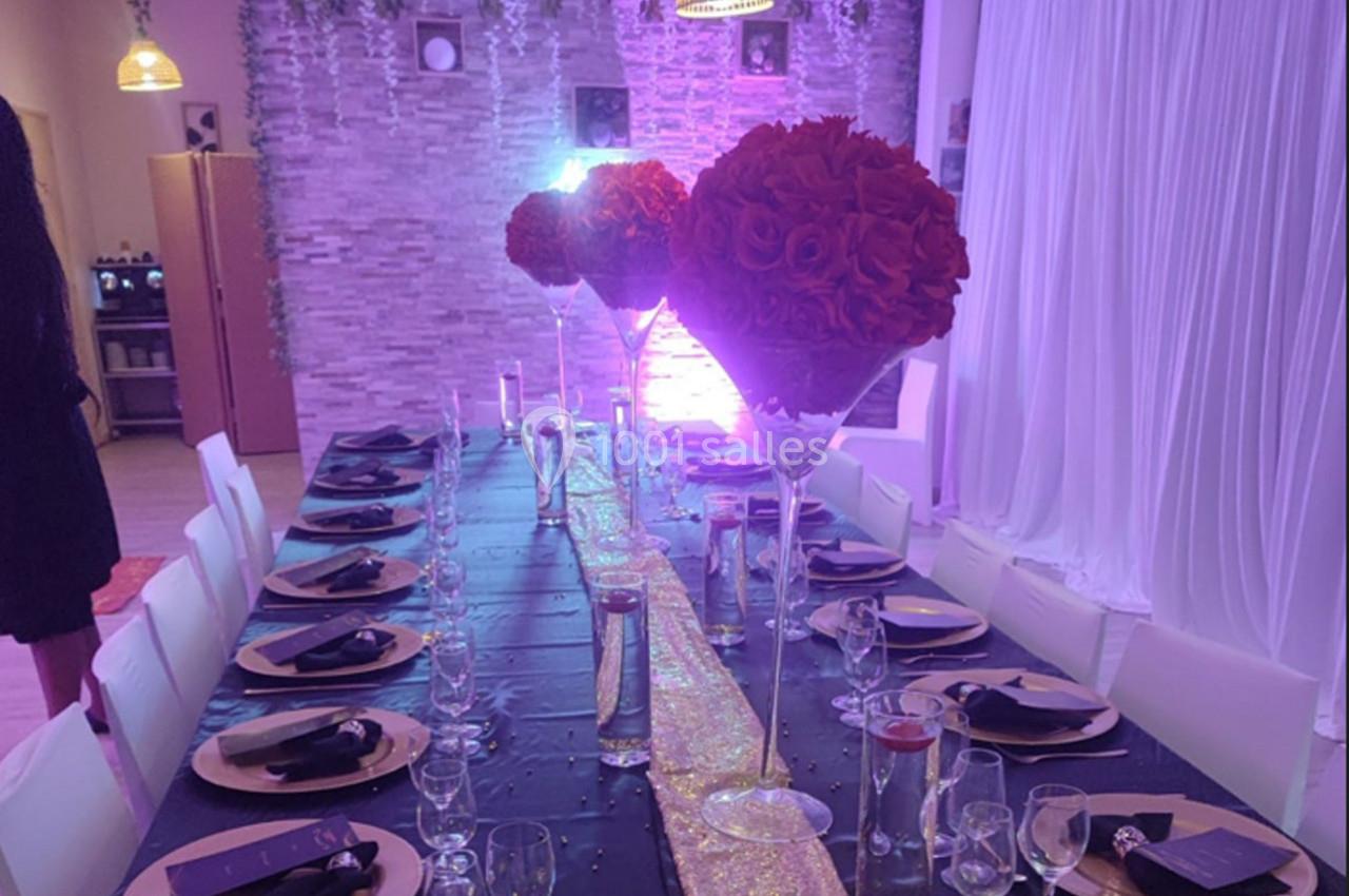 Table décorée pour un événement avec nappes noires, chemins de table dorés, verres et centres de table fleuris rouges.