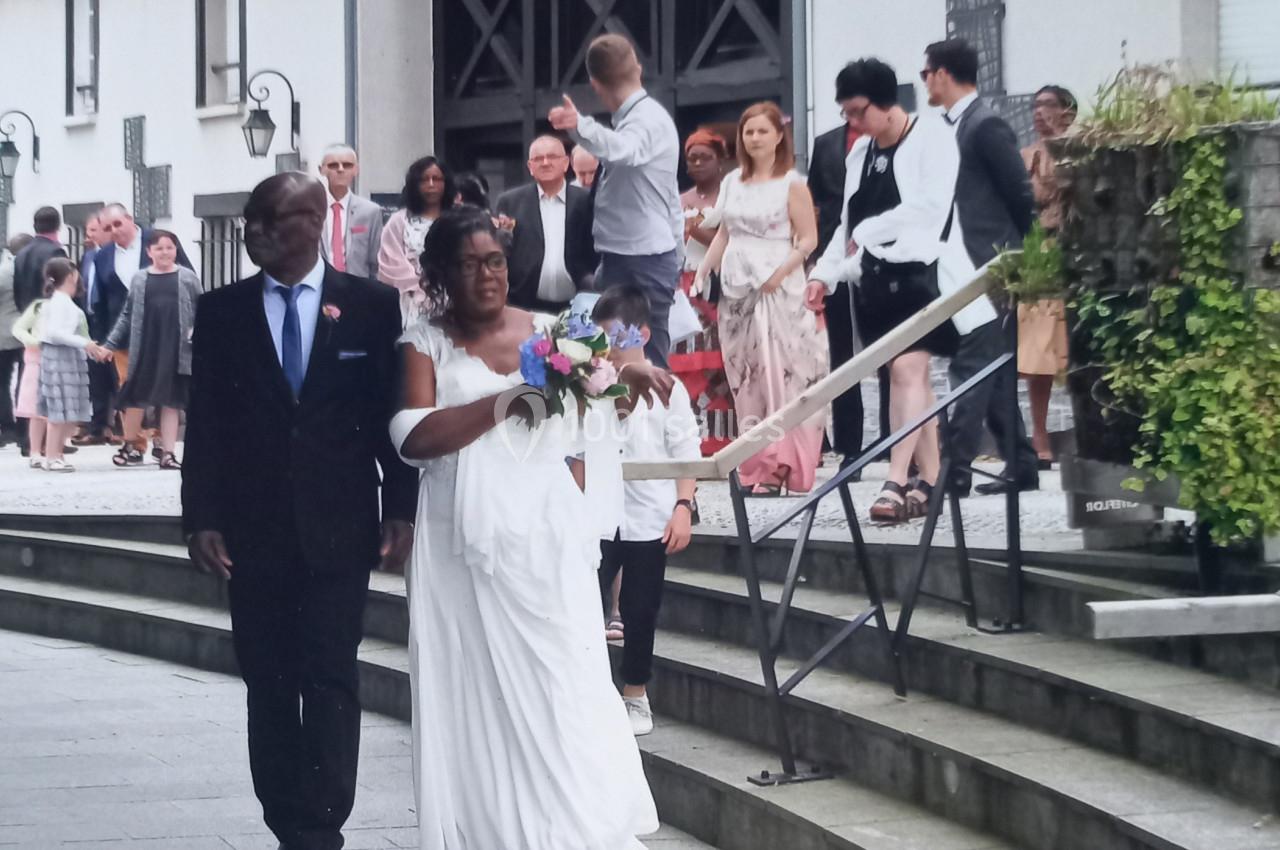 Un couple avance sur des marches devant un bâtiment, entouré d'invités en tenue de cérémonie.