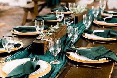 Table élégamment dressée avec nappes blanches, chemins de table verts, serviettes pliées et décorations florales.