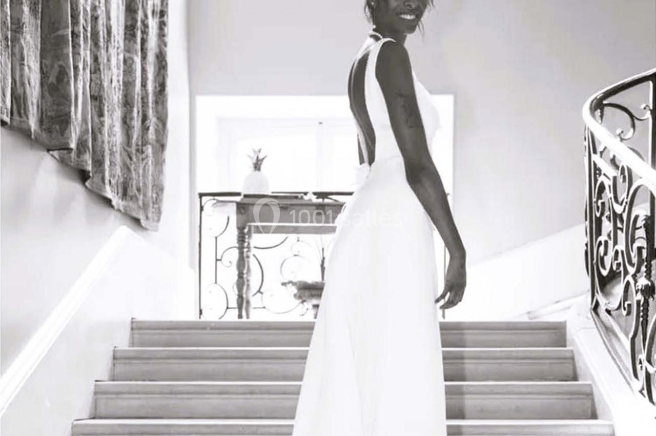 Femme en robe blanche élégante montant un escalier dans un intérieur lumineux, regard tourné vers l'objectif.