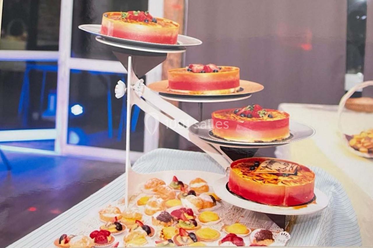 Présentoir avec plusieurs gâteaux colorés et décorés, entourés de petits desserts sur une table.