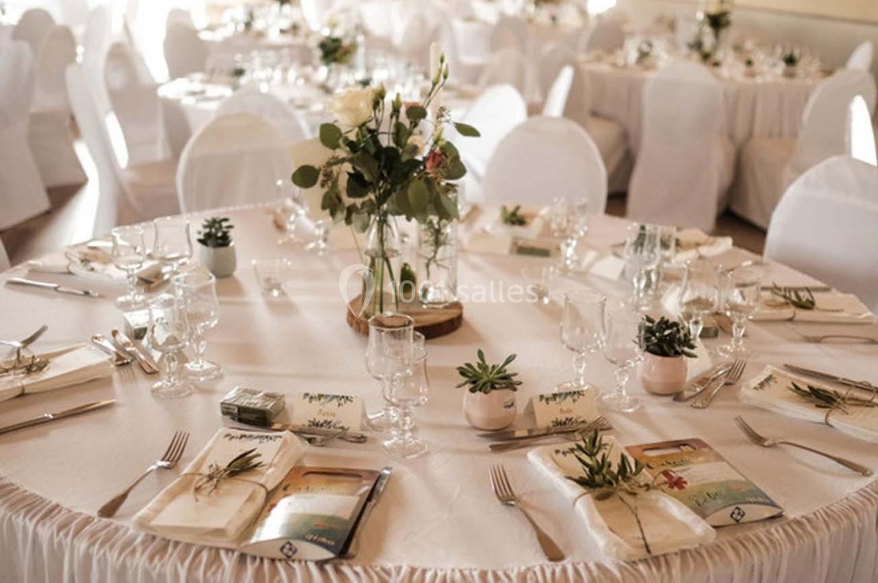 Salle de réception avec tables rondes dressées, nappes blanches, décorations florales et couverts élégants.
