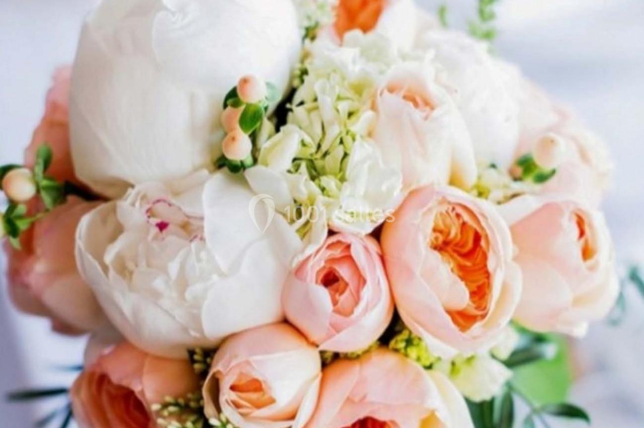 Bouquet de fleurs composé de pivoines blanches, roses saumonées et petites baies, entouré de feuillage vert.