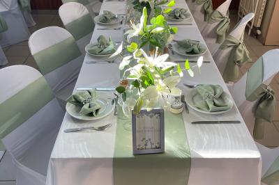Table élégamment dressée avec nappes blanches, chemins de table verts, serviettes pliées et décorations florales.