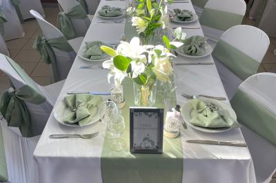 Table élégamment dressée avec nappes blanches, chemins de table verts, serviettes pliées et décorations florales.