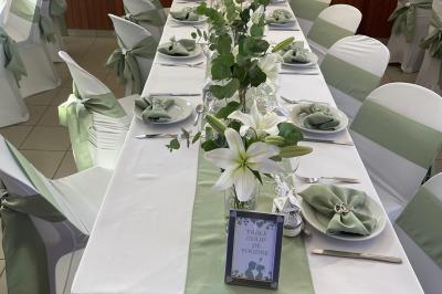 Table élégamment dressée avec nappes blanches, chemins de table verts, serviettes pliées et décorations florales.