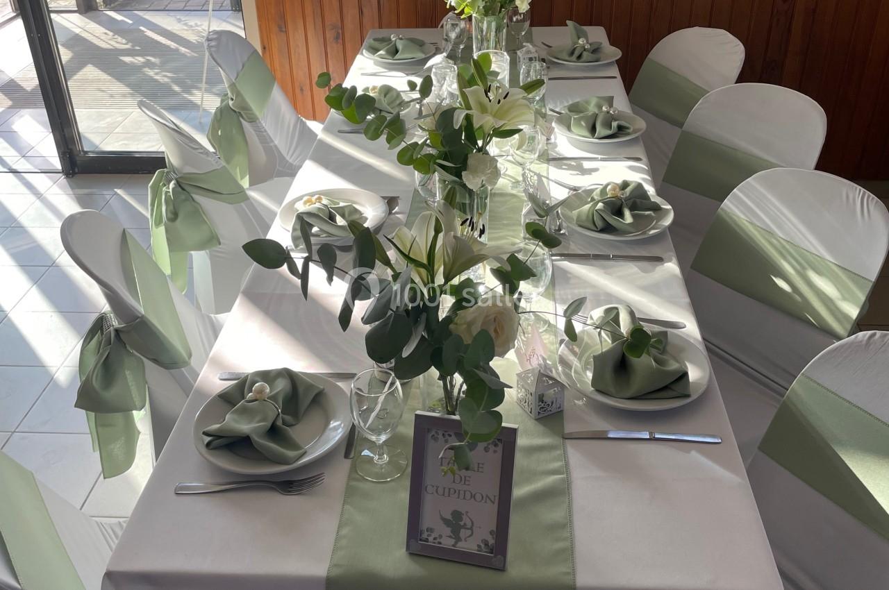 Table élégamment dressée avec nappes blanches, chemins de table verts, serviettes pliées et décorations florales.