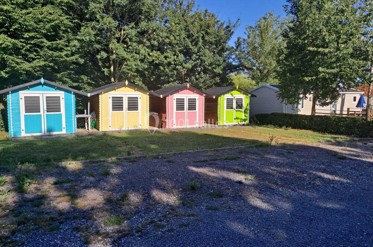 Quatre cabanes colorées alignées devant des arbres, avec une allée en gravier au premier plan.