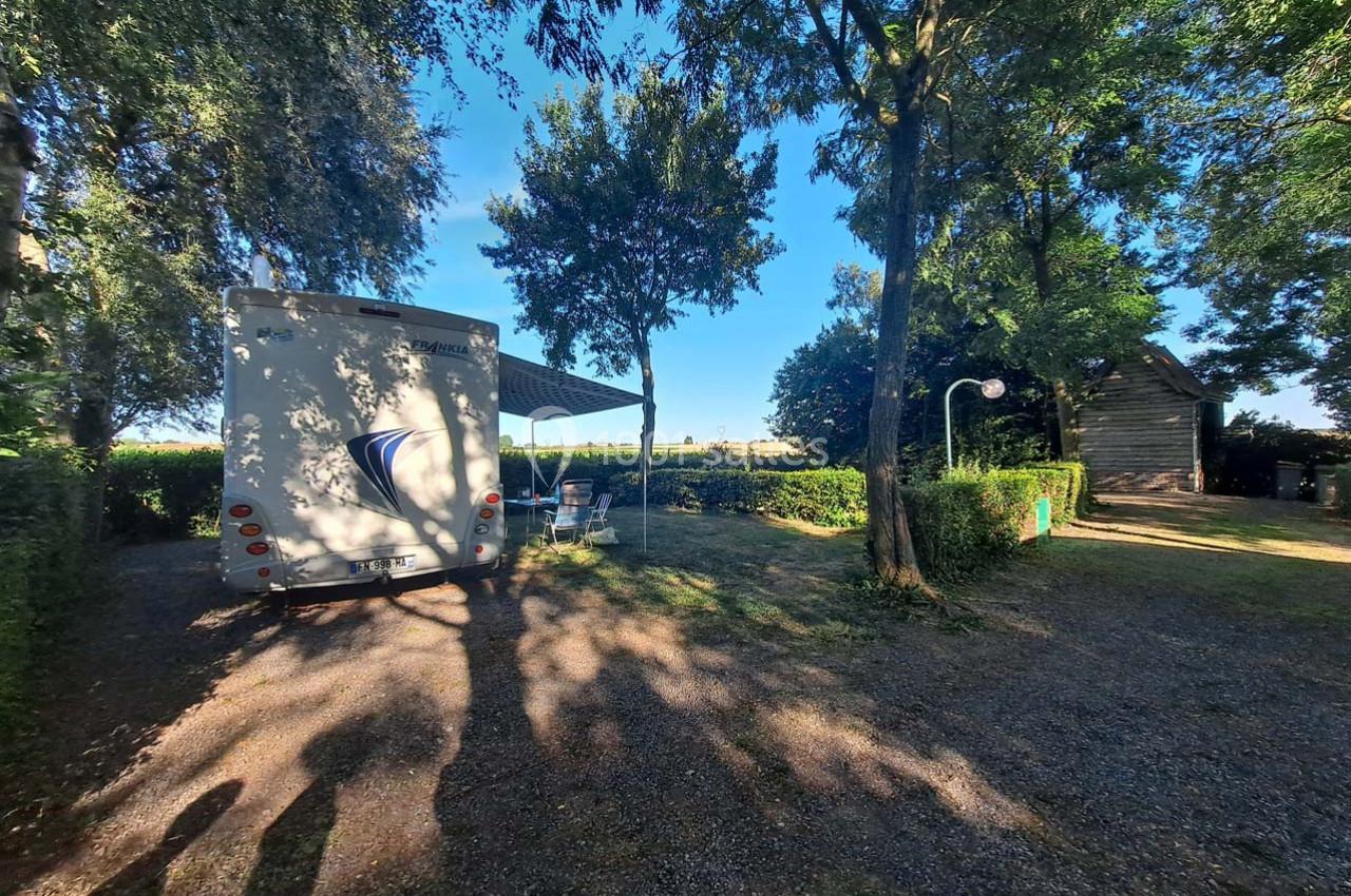 Camping-car stationné sur un emplacement ombragé avec table et chaises, entouré d'arbres et de haies.