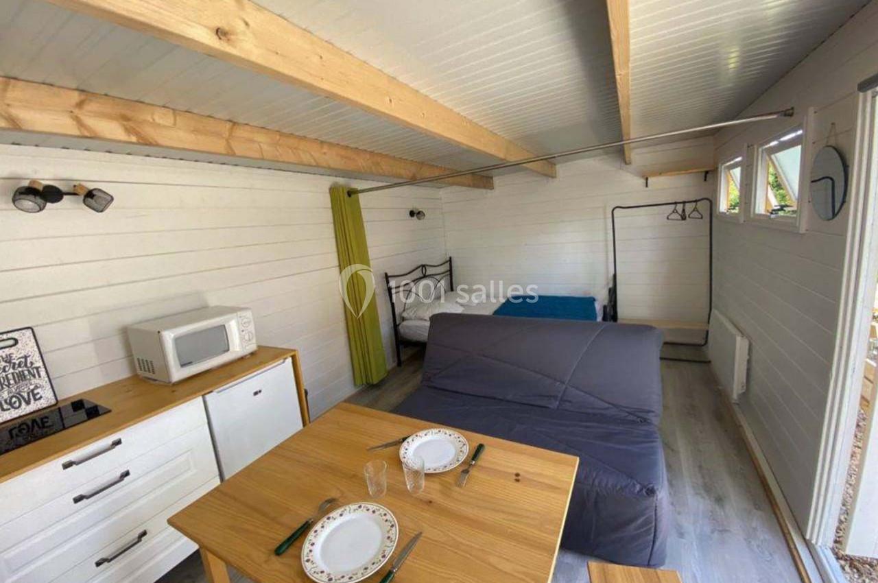 Intérieur d'un petit studio en bois avec lit, canapé, table à manger, kitchenette et lumière naturelle.