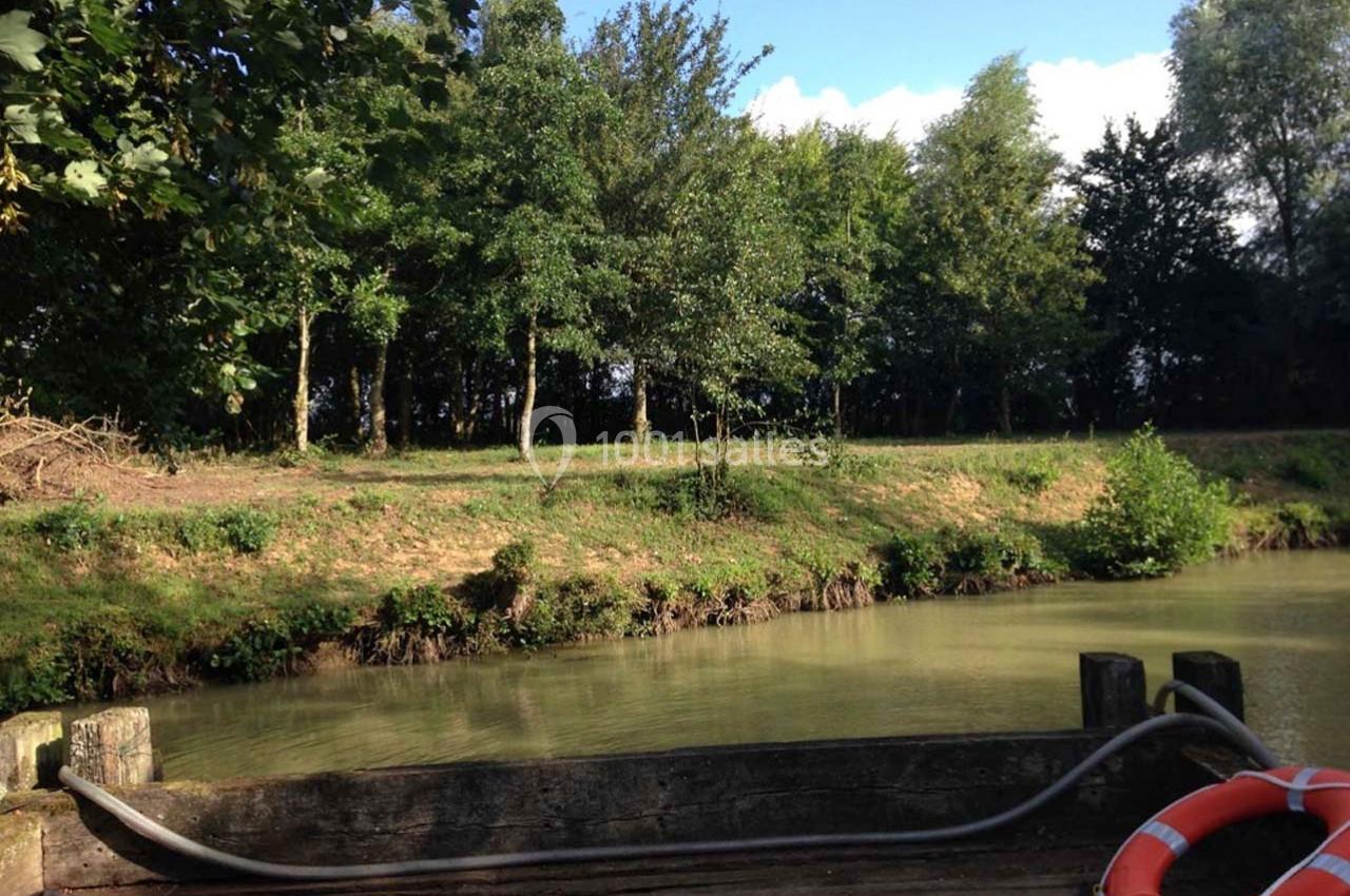 Bord d'un étang entouré d'arbres, vu depuis un ponton en bois avec une bouée de sauvetage posée au sol.