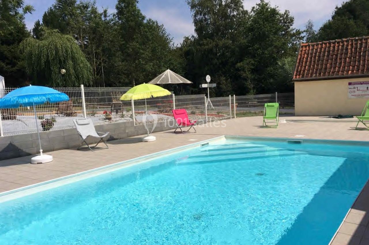 Piscine extérieure avec eau claire, entourée de chaises longues colorées et de parasols, dans un cadre arboré.